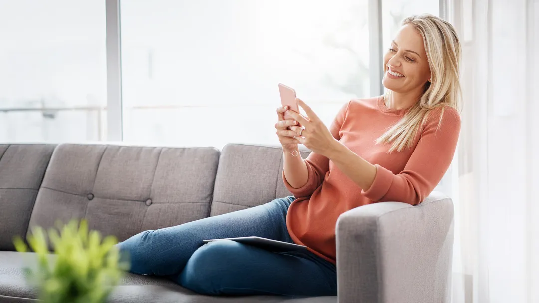 Woman sitting on a couch at home while using a smartphone.