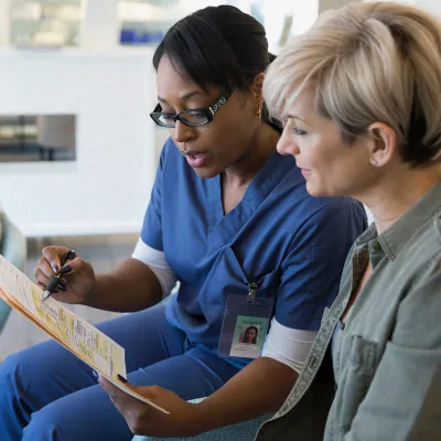 An African American nurse consults with a Caucasian female regarding her diagnosis.