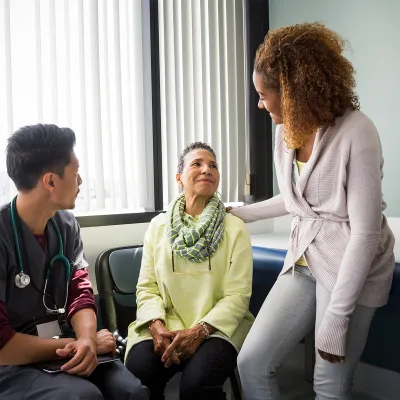 An African American daughter consoles her mother upon hearing medical news from the nurse.